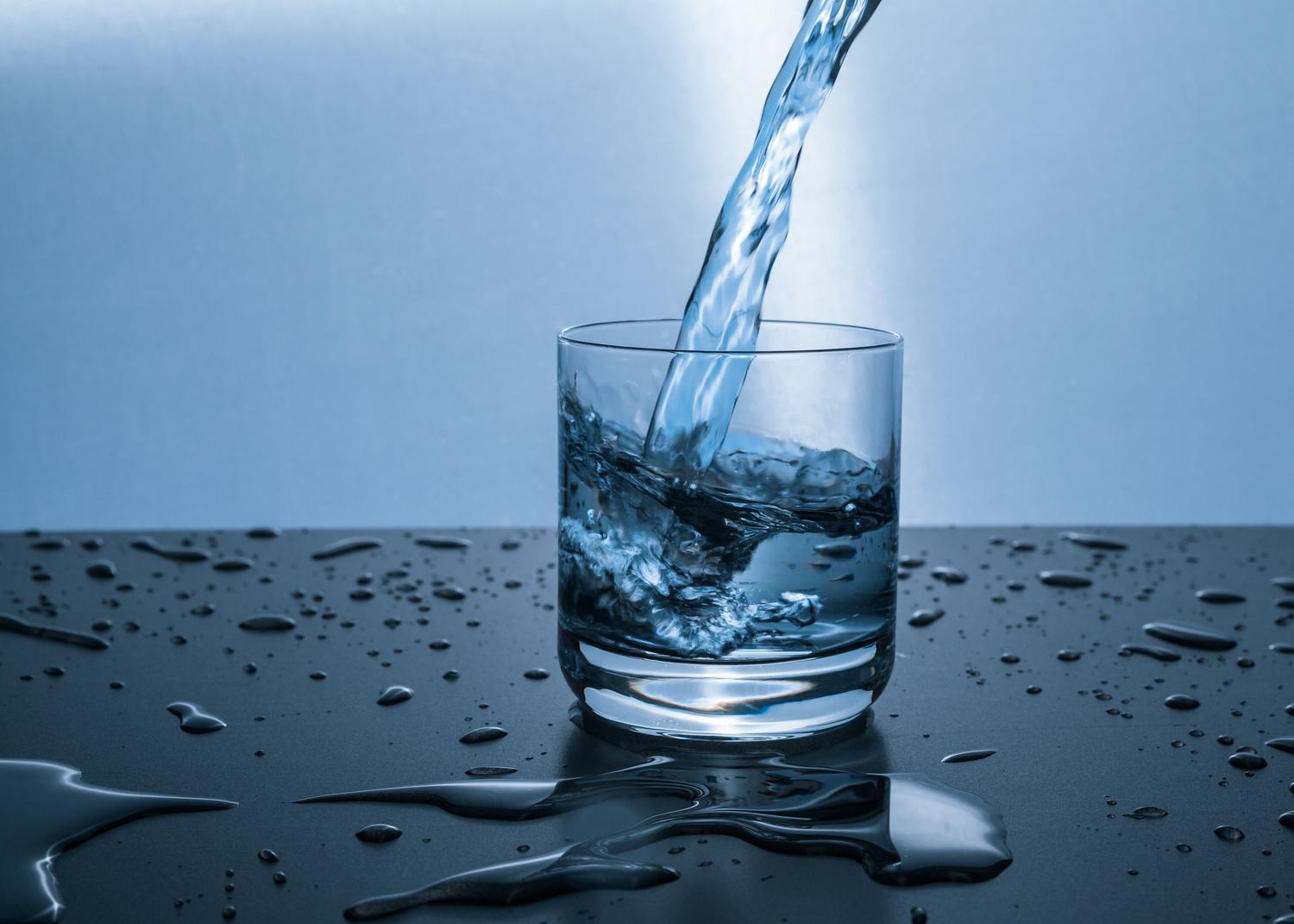 Agua fresca vertiéndose en un vaso de cristal, representando la importancia de la hidratación para combatir la retención de líquidos.