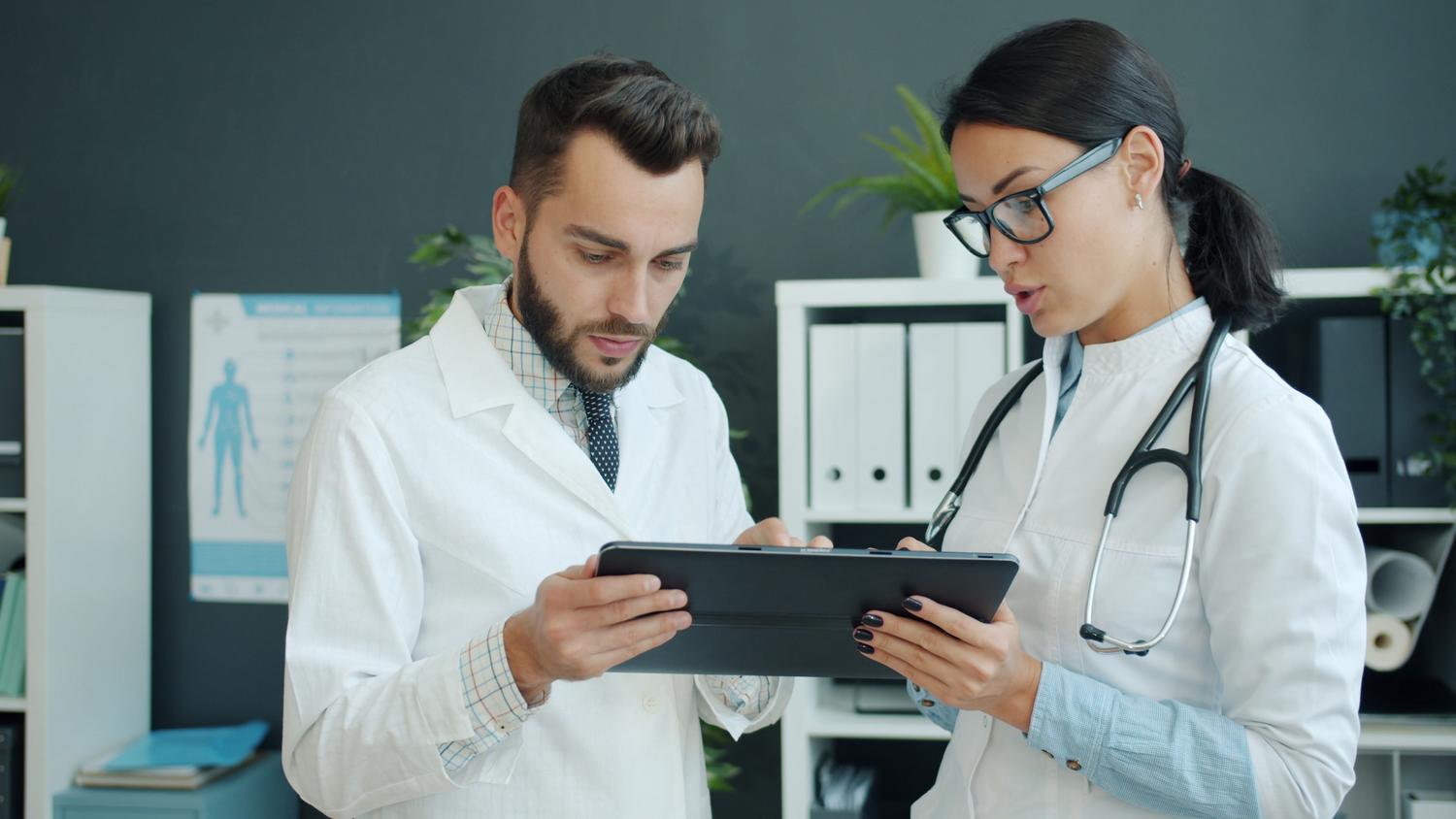 Dos profesionales de la salud analizando datos médicos en una tablet, ilustrando el trabajo de la enfermería informática.
