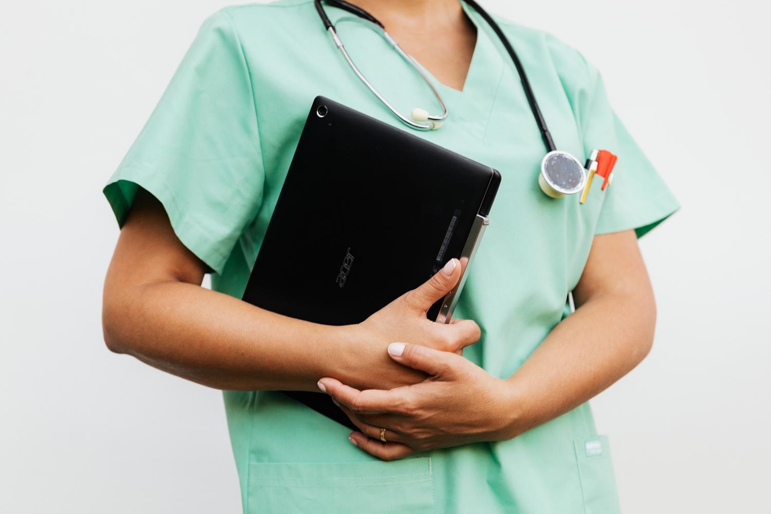Enfermera con uniforme quirúrgico sosteniendo una tablet y un estetoscopio, representando la integración de la tecnología en el cuidado clínico.