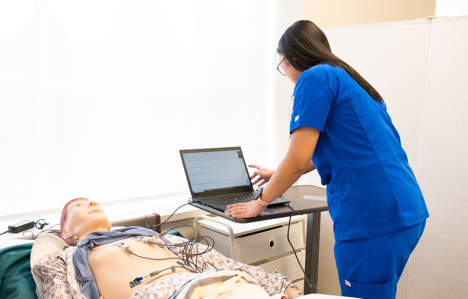 Estudante de enfermagem em um laboratório de simulação com um manequim médico, ilustrando a formação prática e o uso de tecnologia educativa.