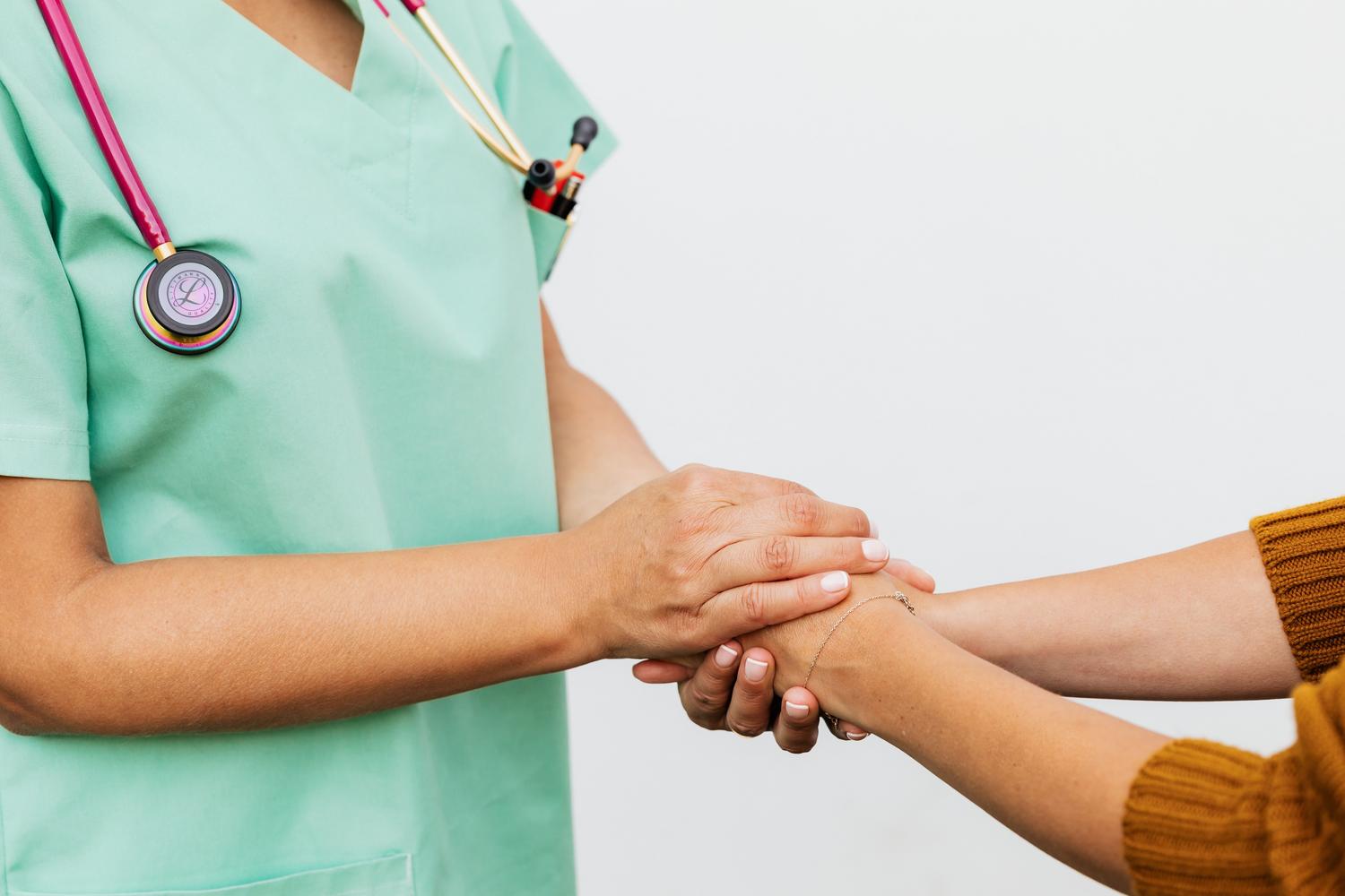 Primeiro plano de um médico segurando as mãos de um paciente, simbolizando a empatia, a humanização e o vínculo ético na medicina.