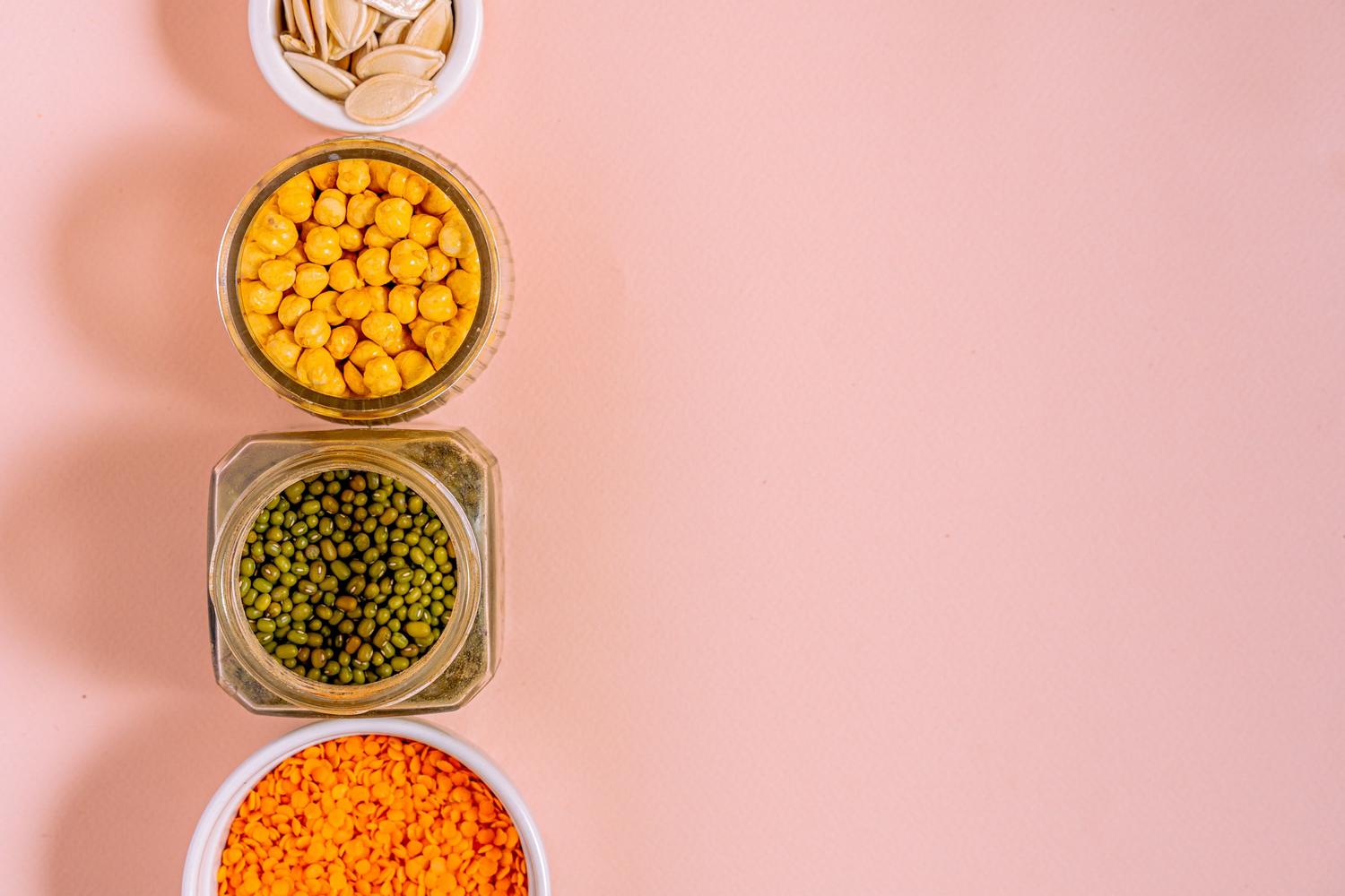 Composición visual de garbanzos, lentejas y semillas sobre un fondo rosa suave, aportando variedad estética a las fuentes de legumbres.