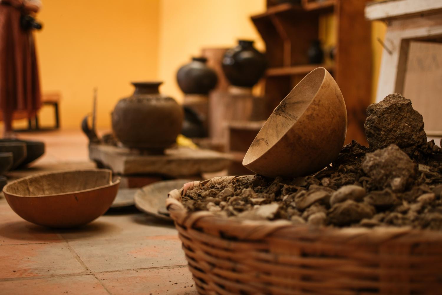 Recipientes de cerámica rústica junto a tierra arcillosa bruta, simbolizando la transformación de la materia prima natural en herramientas útiles.