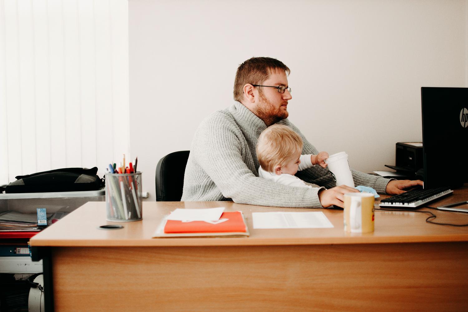 Padre trabajando desde casa mientras cuida de su hijo, simbolizando la conciliación entre la vida profesional y la familiar.