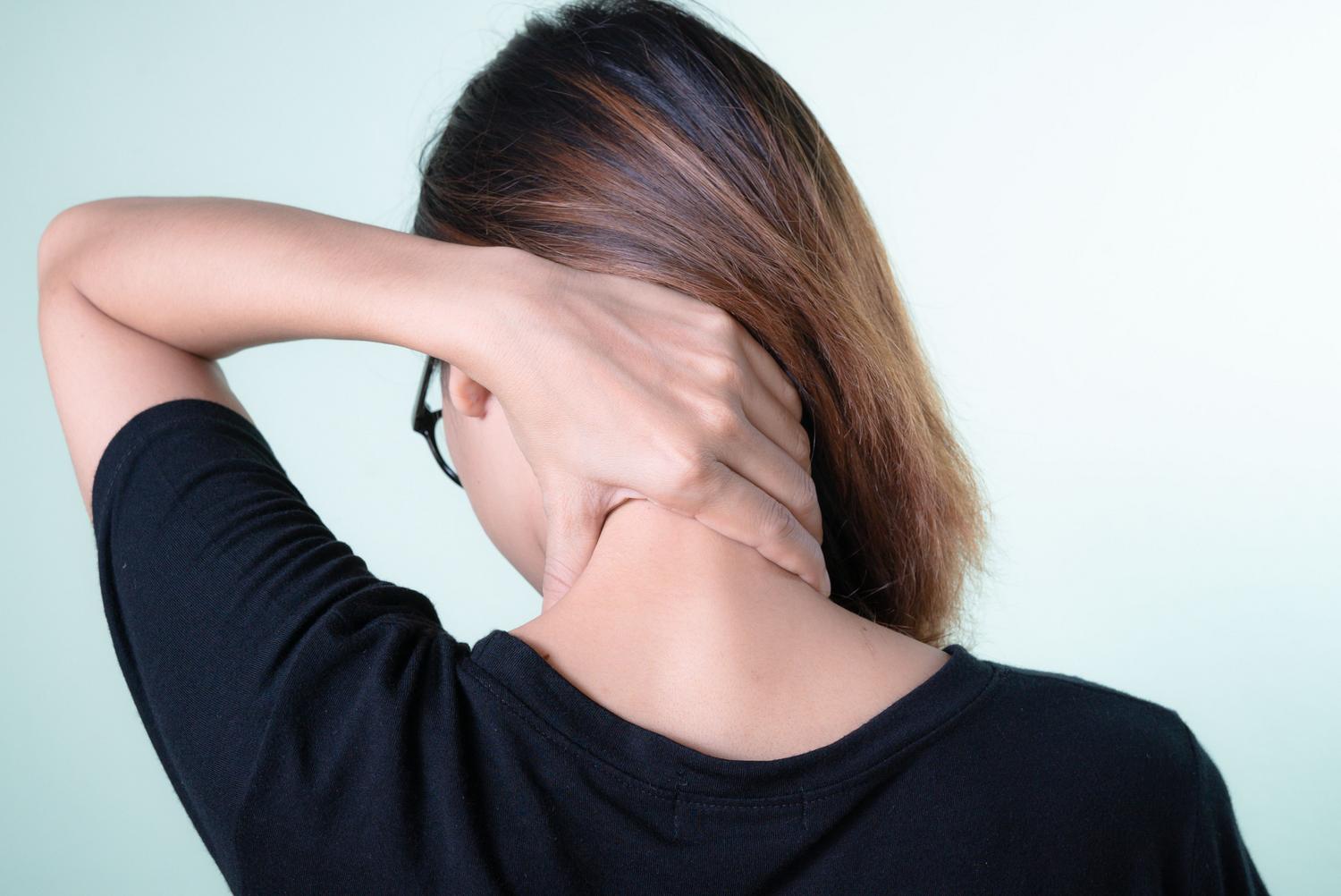 Vista posterior de una mujer masajeando su propio cuello debido a la rigidez