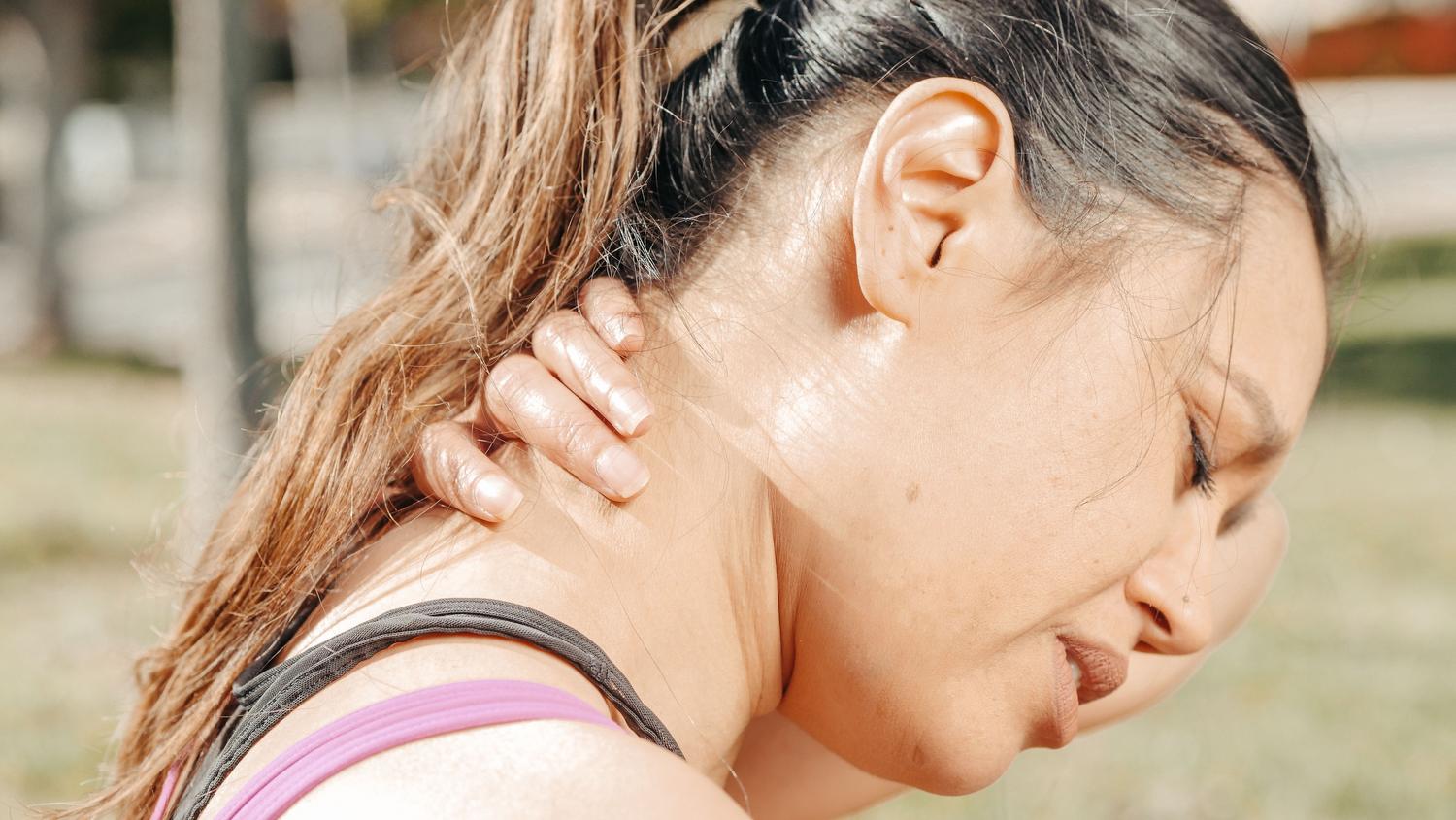 Mujer agarrándose el cuello con expresión de dolor y tensión cervical