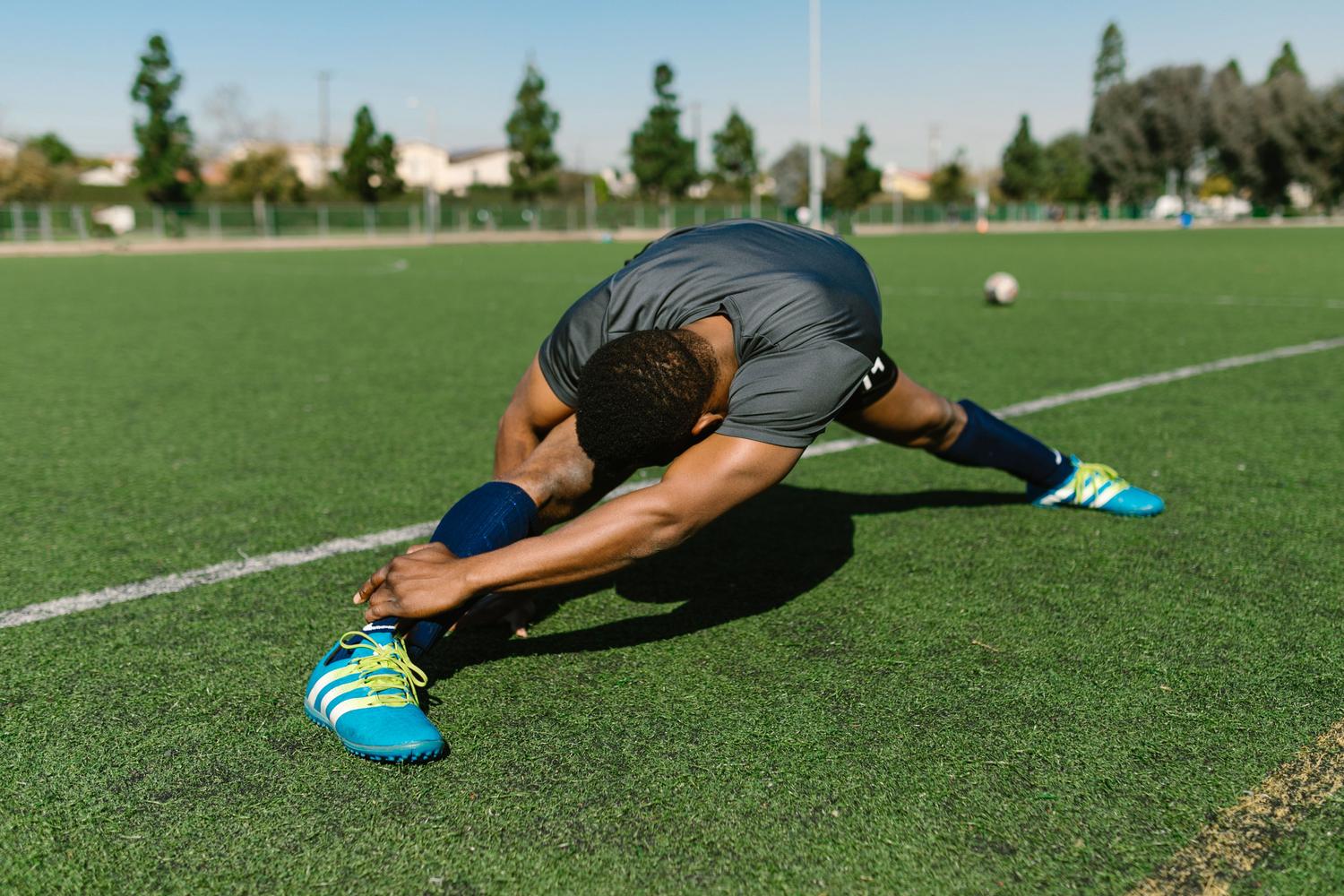 Atleta realizando estiramientos en un campo de fútbol como parte de una estrategia de prevención de lesiones. Atleta realizando estiramientos en un campo de fútbol como parte de una estrategia de prevención de lesiones.