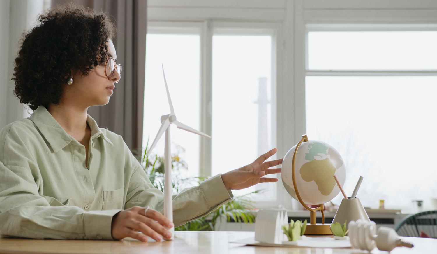 Mujer profesional analizando un globo terráqueo y una maqueta de turbina eólica, representando la visión estratégica para un futuro sostenible.