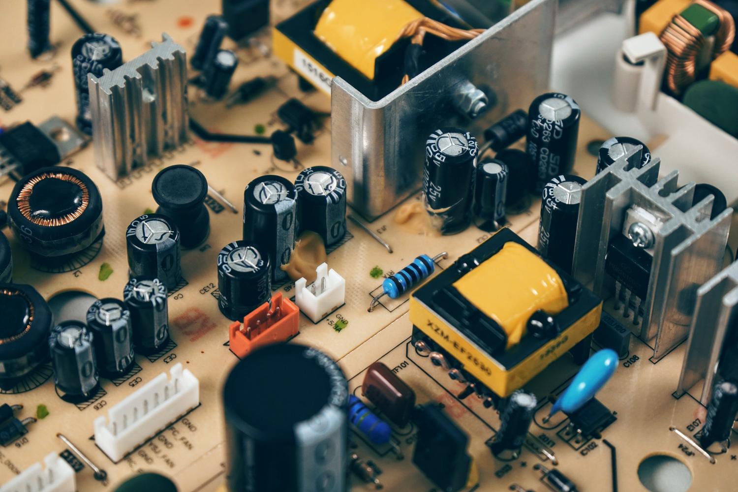 Primer plano de um transistor negro junto a um condensador em uma placa de circuito, ideal para ilustrar o componente físico do transistor.