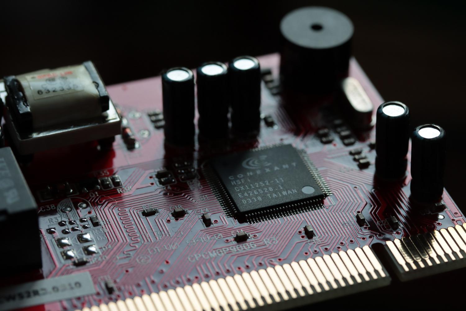 Vista detallada de una placa de circuito rojo con diversos componentes electrónicos y un microchip, representando la base de la electrónica digital.