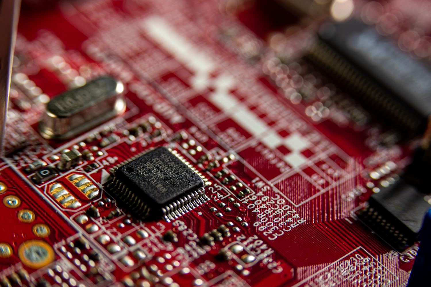 Fotografía macro de una placa de circuito rojo resaltando la miniaturización de los componentes electrónicos.