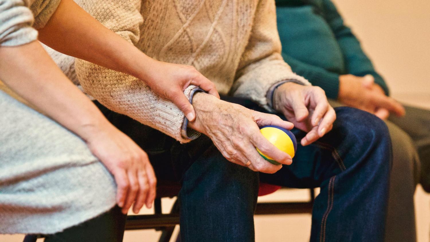 Primer plano de las manos de un cuidador brindando apoyo y estimulación sensorial a un paciente com Alzheimer.