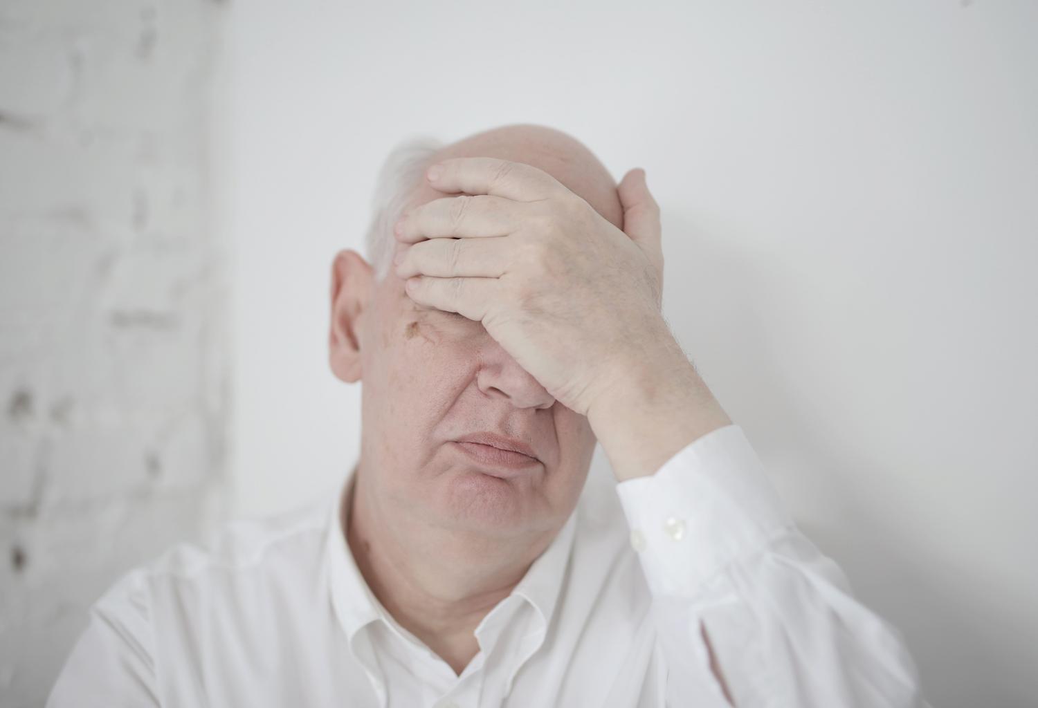 Hombre mayor cubriéndose el rostro con la mano, ilustrando la frustración y los cambios de humor asociados al Alzheimer.