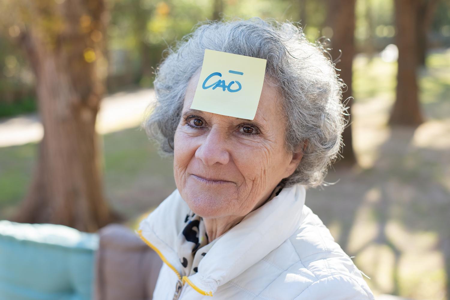 Mujer mayor con una nota adhesiva en la frente, simbolizando la pérdida de memoria y el uso de recordatorios en el Alzheimer.