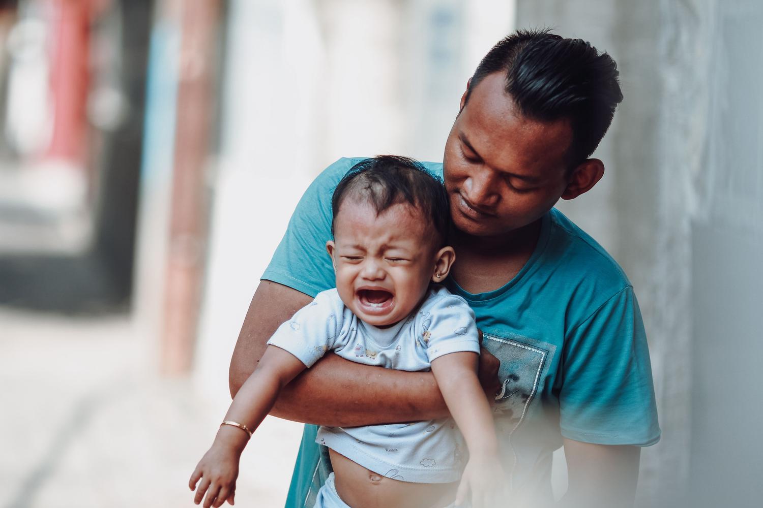 Padre consolando a su hijo pequeño mientras llora, ilustrando la importancia de validar las emociones infantiles.