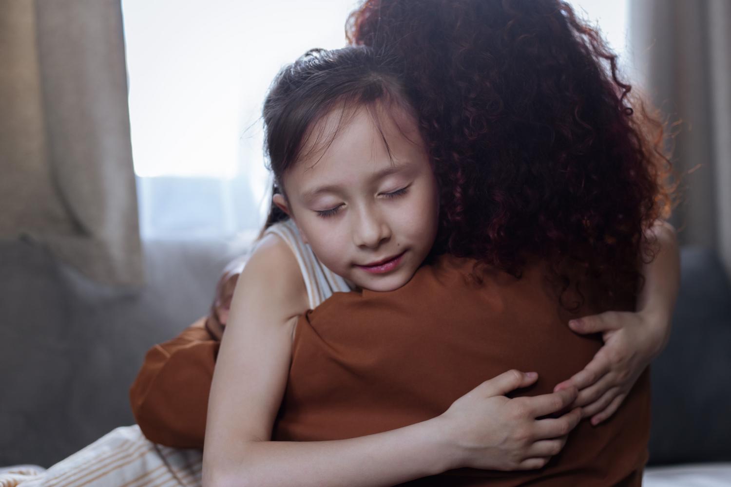 Abrazo sentido entre madre e hija en el interior de un hogar, simbolizando conexión emocional y seguridad.