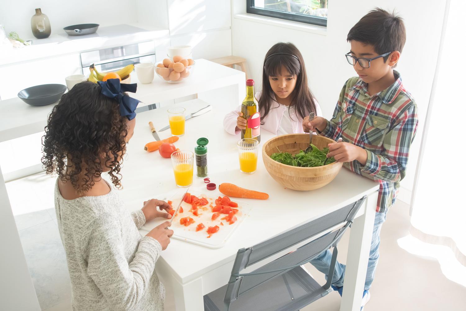 Grupo de niños preparando juntos una ensalada de verduras frescas en la cocina, promoviendo la diversidad nutricional.