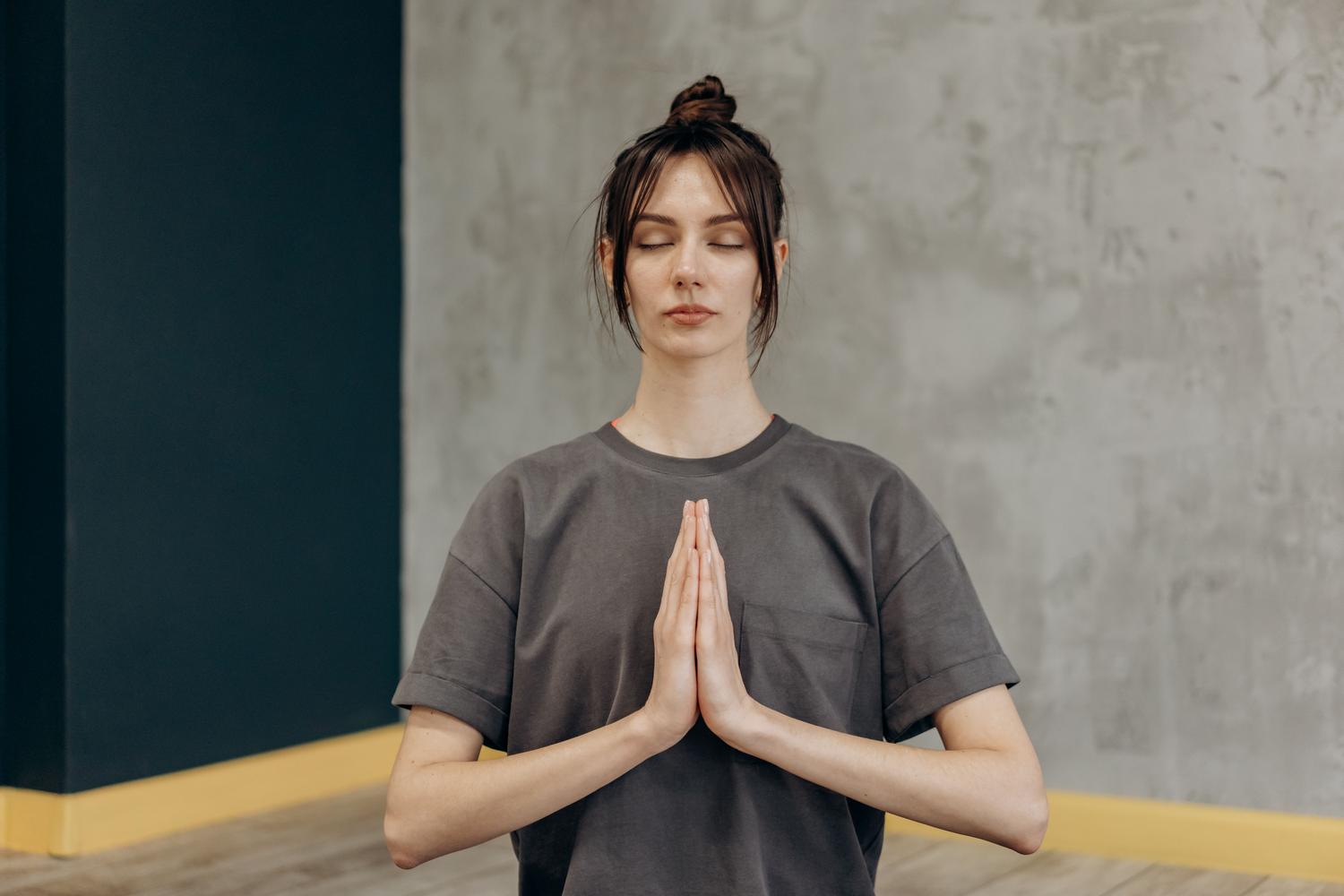 Mujer meditando con los ojos cerrados y las manos en posición de oración para encontrar la paz interior y el mindfulness