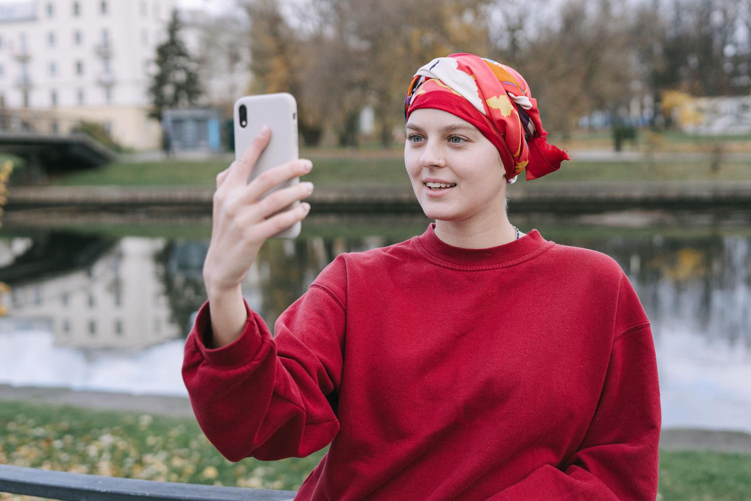 Mujer joven con pañuelo rojo sonriendo durante una videollamada al aire livre, transmitindo resiliência e esperança.