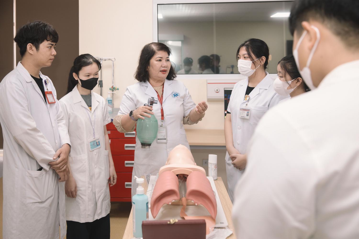 Grupo de estudiantes de medicina en una sesión de formación práctica guiada por una instructora con un maniquí de entrenamiento.