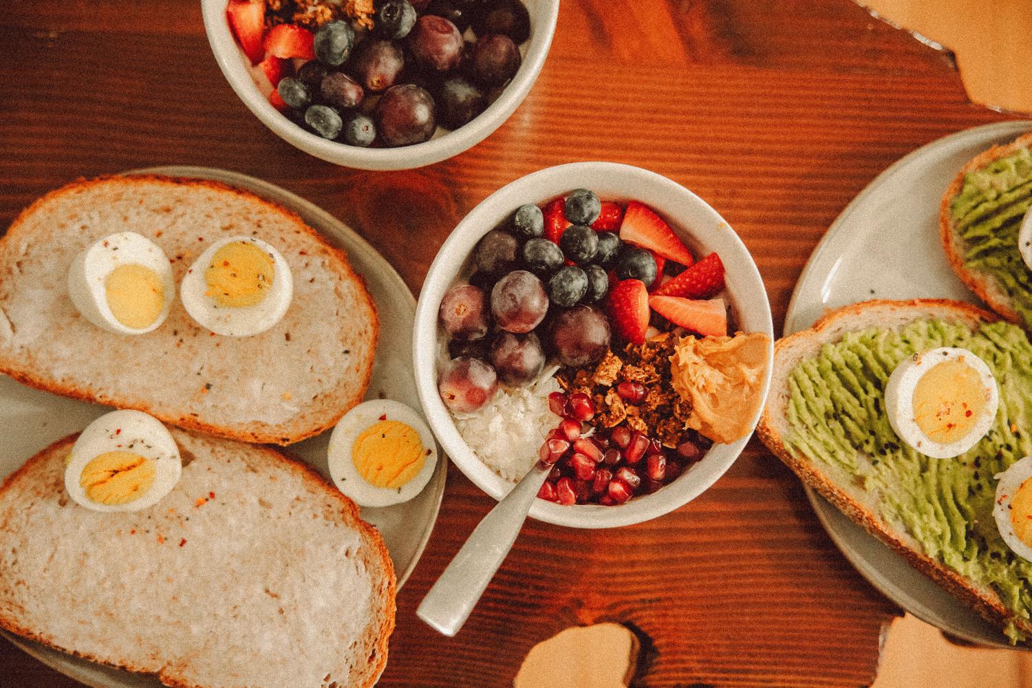 Desayuno saludable variado con bowl de yogur y frutas, y tostadas de aguacate con huevo.