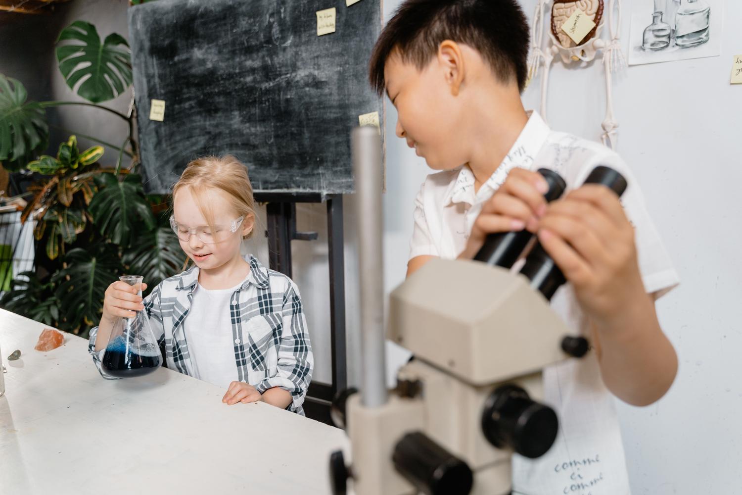 Dos niños utilizando un microscopio y matraces en un laboratorio, explorando conceptos de biología.