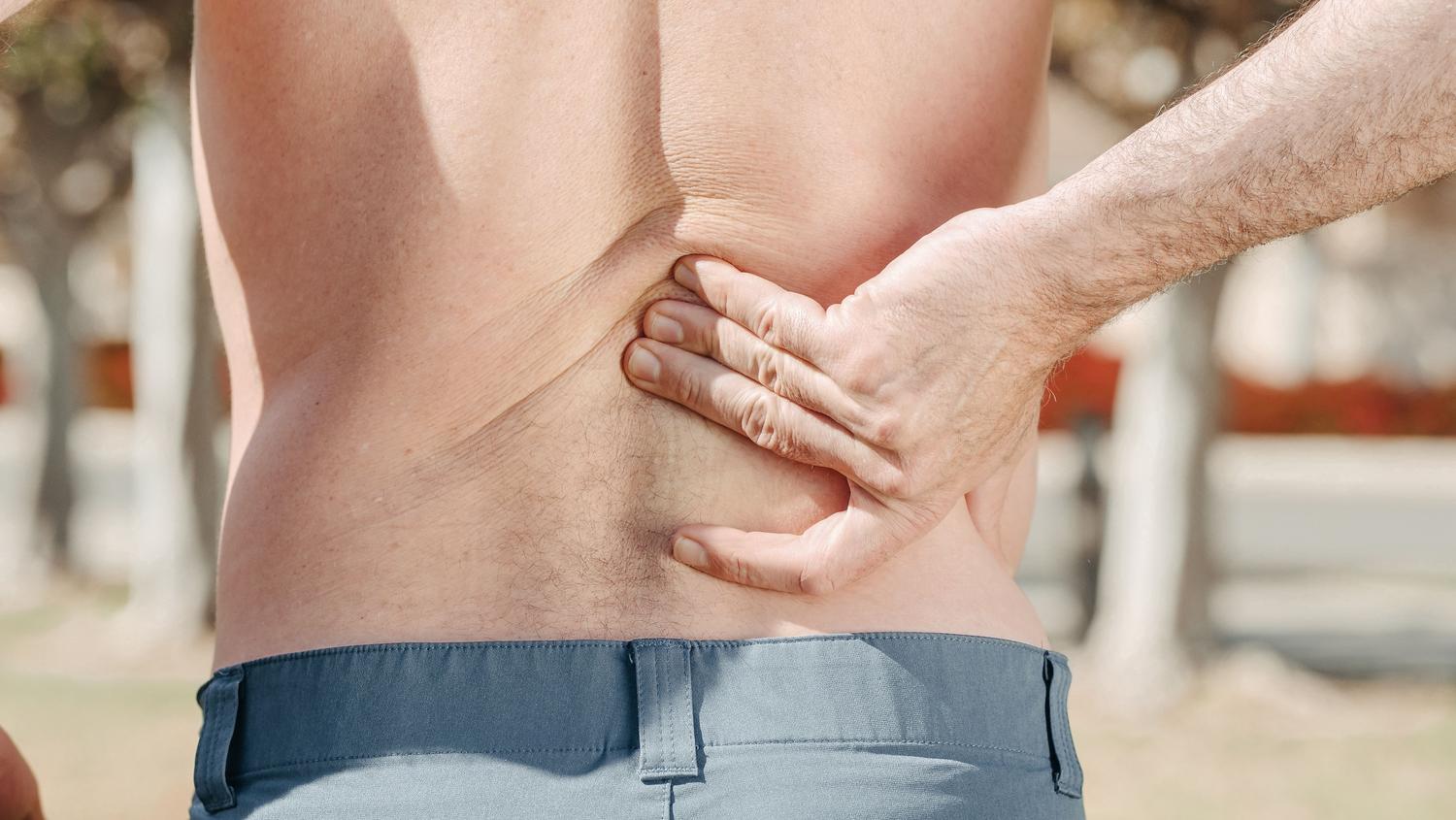 Primer plano de un hombre sosteniendo su zona lumbar debido al dolor de espalda.