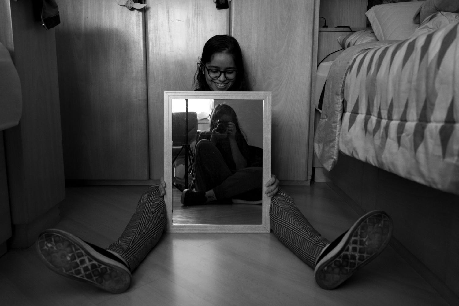 Fotografía en blanco y negro de una mujer sosteniendo un espejo y capturando su propio reflejo, simbolizando la autoexploración y la búsqueda de identidad.