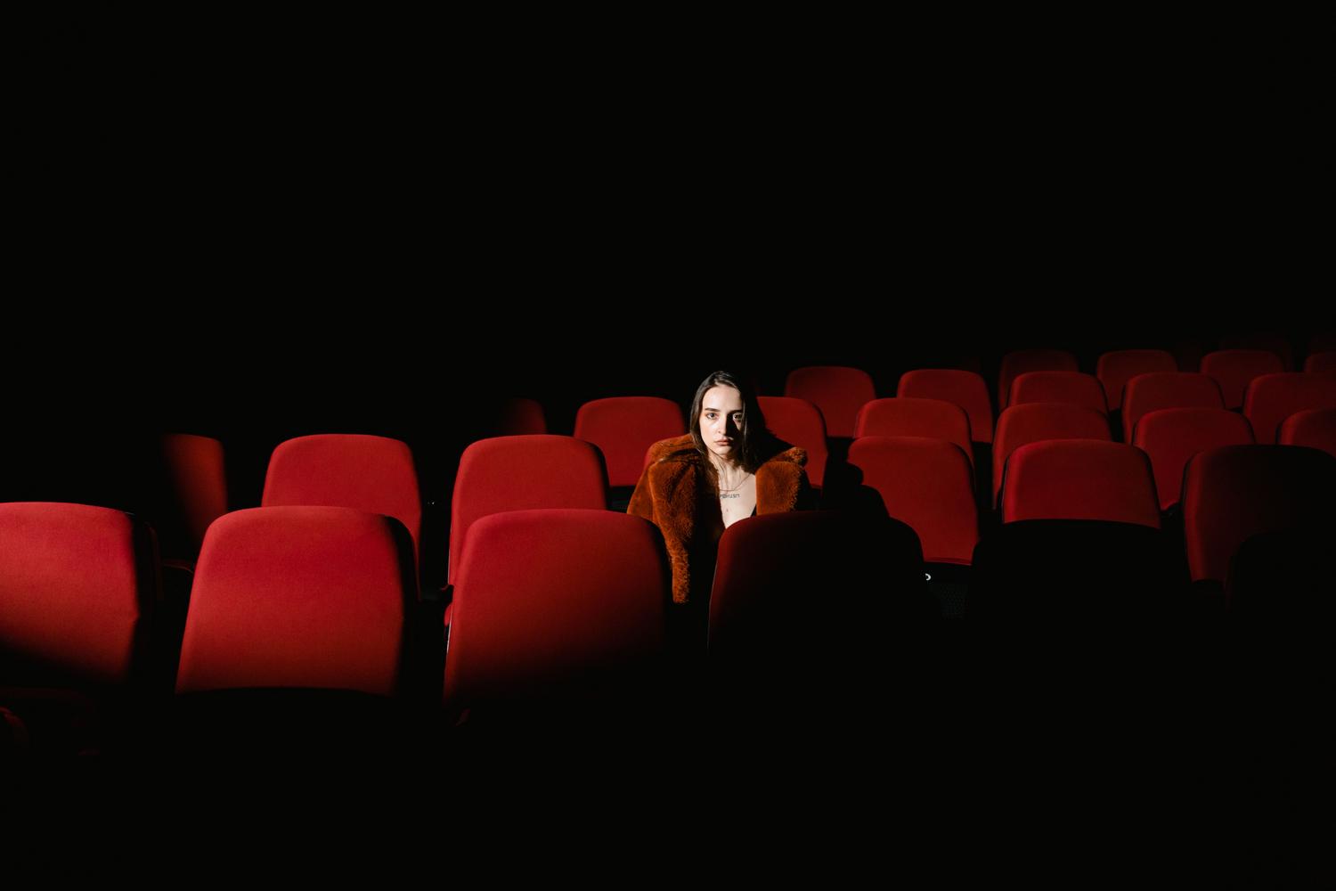 Mujer sentada sola en una sala de cine oscura, evocando introspección y reflexión.