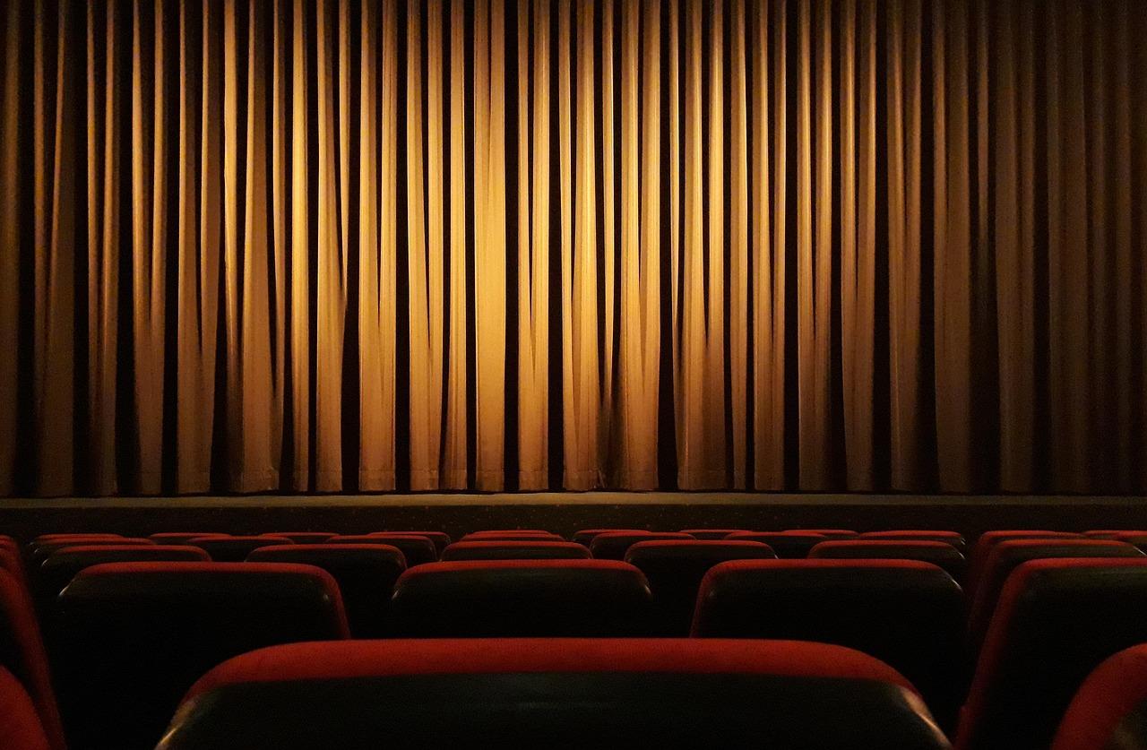 Vista de un cine vacío con asientos rojos y telón dorado, creando una atmósfera cinematográfica clásica.