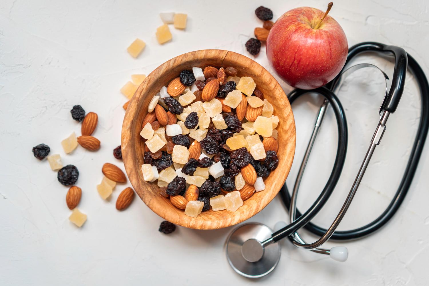 Cuenco con frutos secos y frutas deshidratadas junto a un estetoscopio, simbolizando la dieta saludable para prevenir riesgos cardiovasculares.