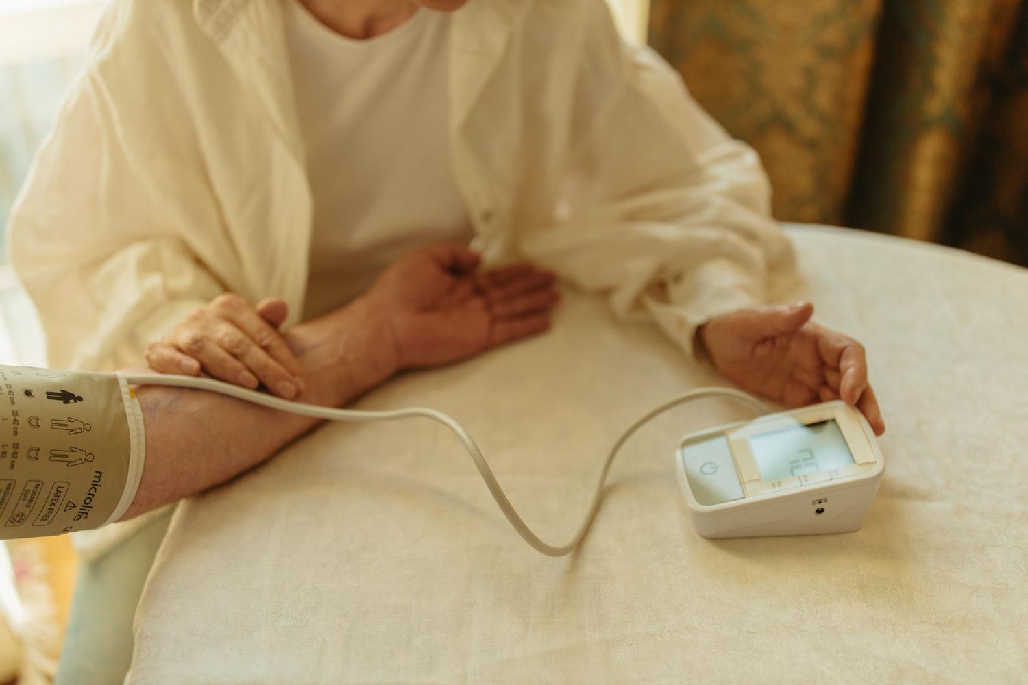 Persona mayor midiendo su presión arterial en casa con un monitor digital, representando la automedición para detectar la hipertensión enmascarada.