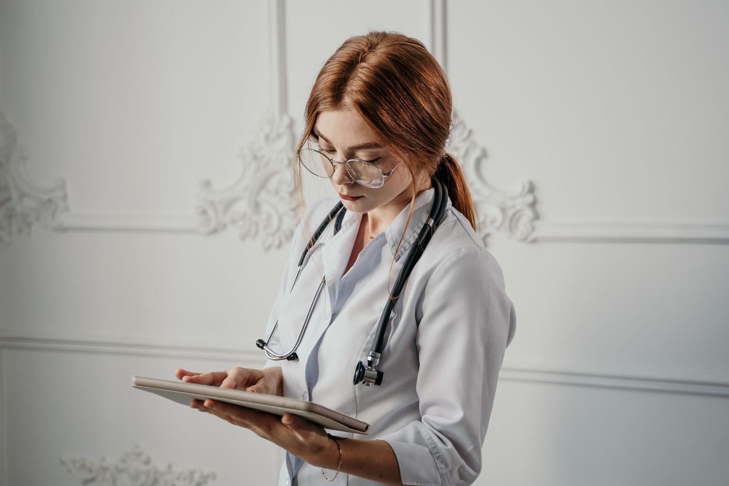 Médica utilizando una tablet en un entorno clínico moderno, representando la digitalización de la salud y el acceso móvil a datos.