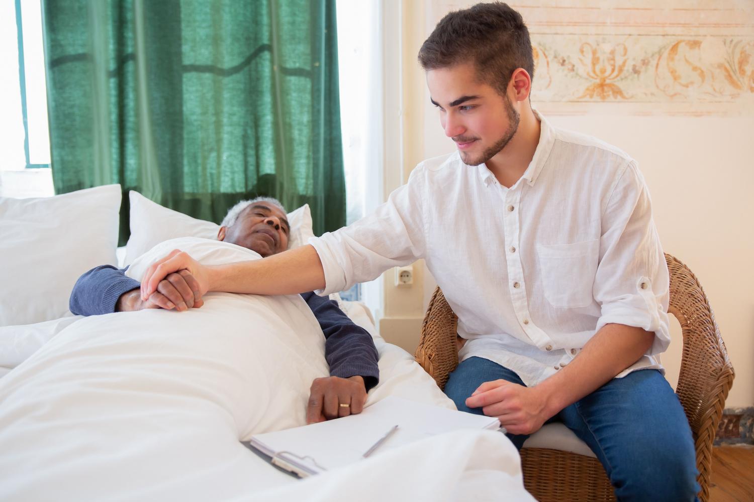 Profesional de salud brindando apoyo emocional y físico a un paciente anciano en cama, reflejando la empatía y la dignidad en los cuidados paliativos.