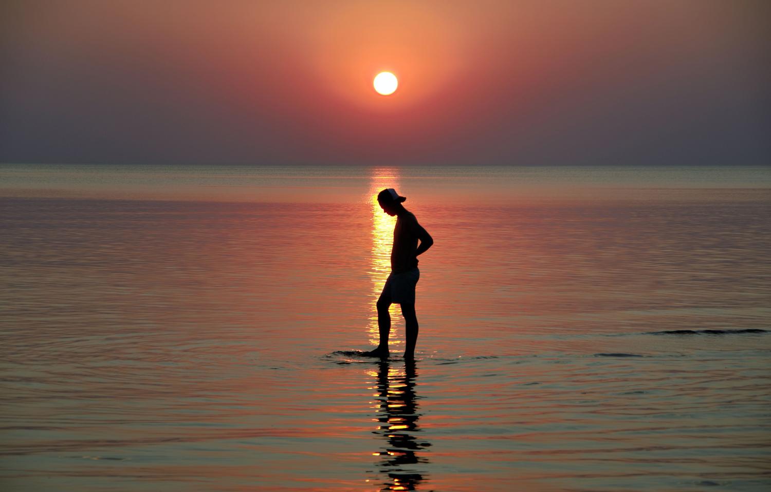 Silueta serena de una persona caminando por el agua durante el atardecer, evocando calma y la positividad de la solitude.