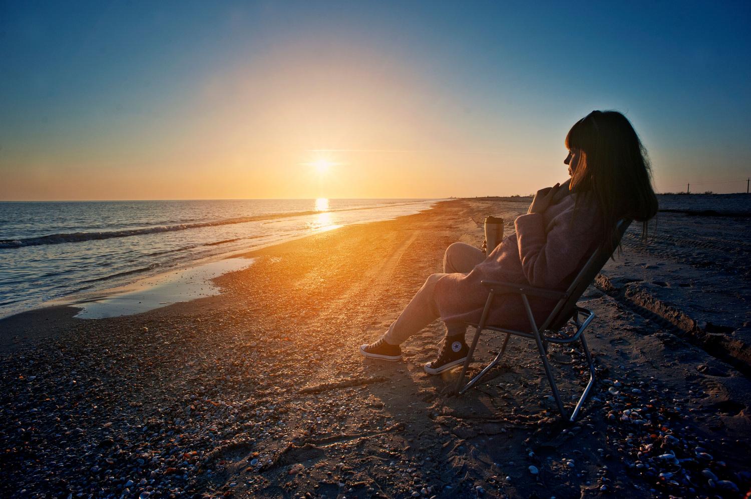 Mujer relajada en una silla de playa disfrutando de un atardecer, representando la autonomía y el placer de la propia compañía. Mujer relajada en una silla de playa disfrutando de un atardecer, representando la autonomía y el placer de la propia compañía.