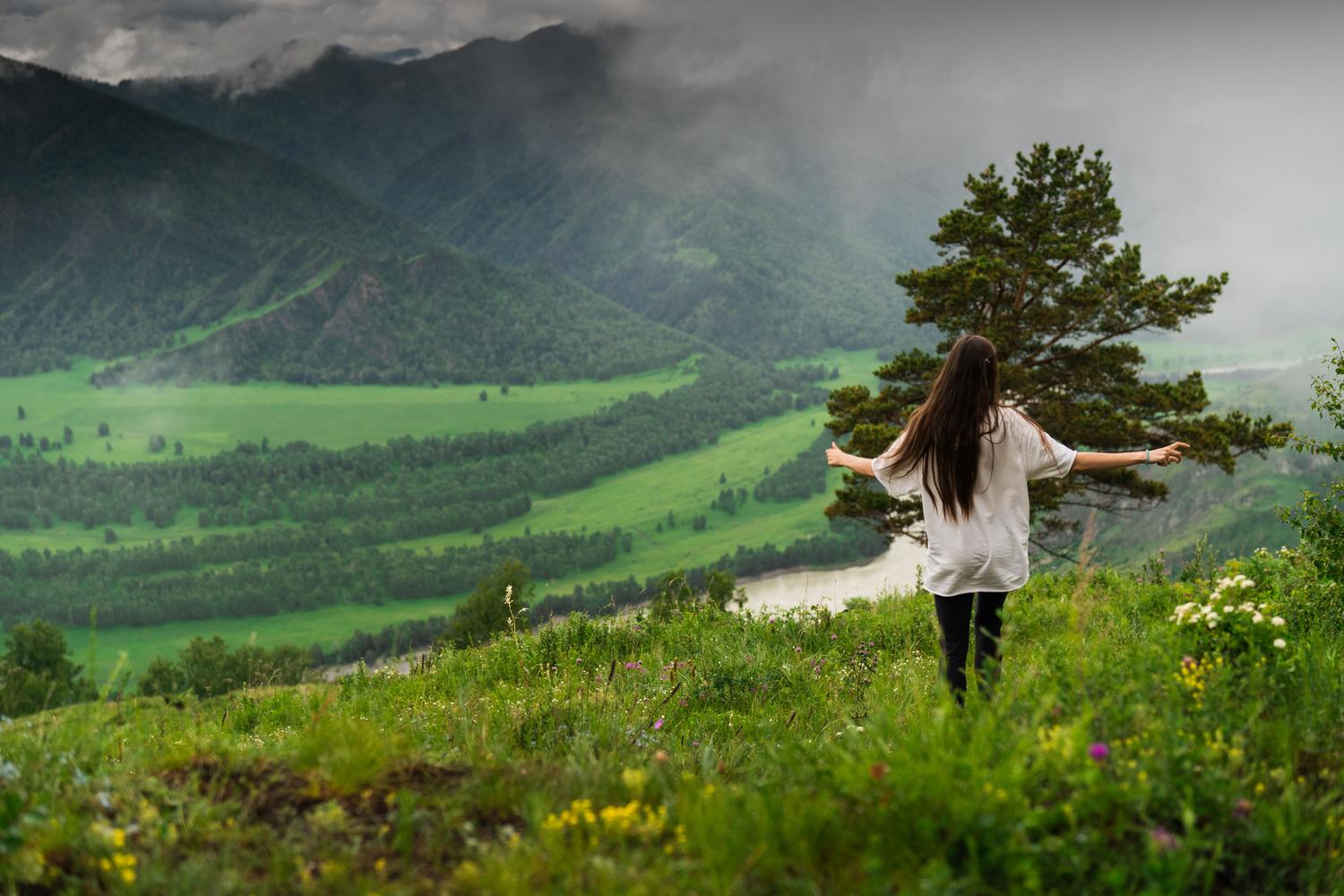 Mujer con los brazos abiertos en un valle verde y montañoso, transmitiendo libertad y conexión vital con la naturaleza.