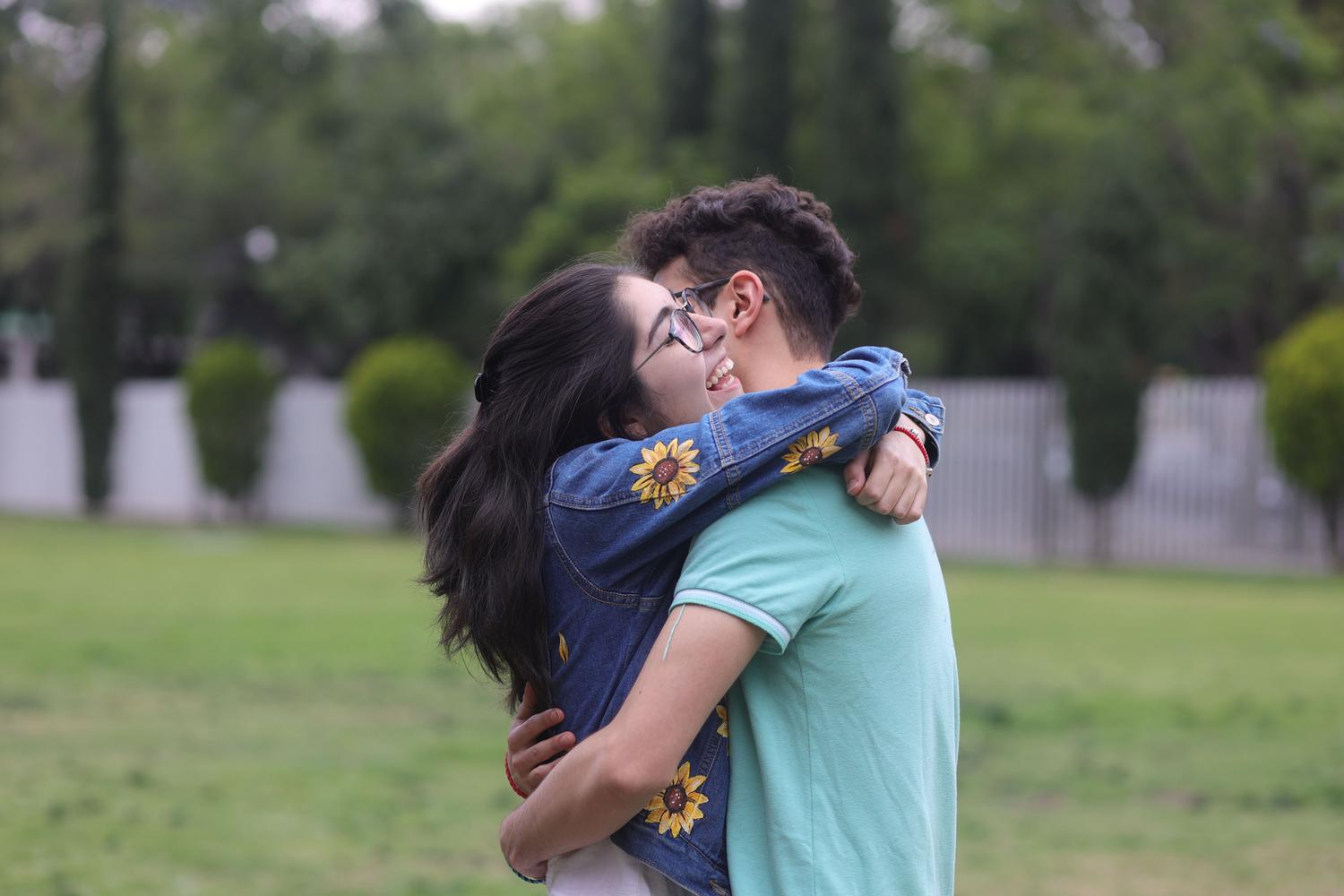 Pareja joven compartiendo un abrazo afectuoso en un parque verde, representando el amor verdadero y la complicidad.