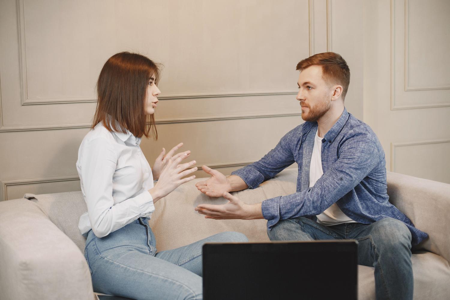 Pareja joven sentada en un sofá manteniendo una conversación reflexiva, ilustrando la importancia de la comunicación y la inteligencia emocional.
