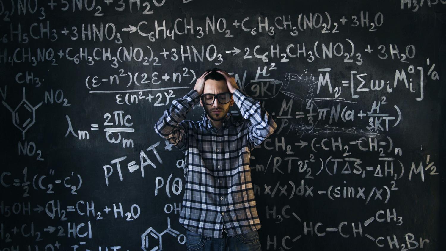 Profesor de ciencias con expresión de agotamiento y estrés frente a una pizarra llena de fórmulas complejas, representando el burnout docente.