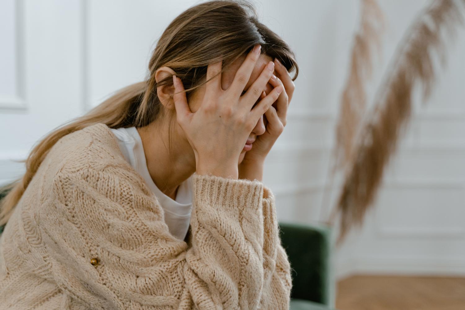 Mujer sentada cubriéndose el rostro en un gesto de frustración y estrés, representando el caos mental de la psicosis puerperal