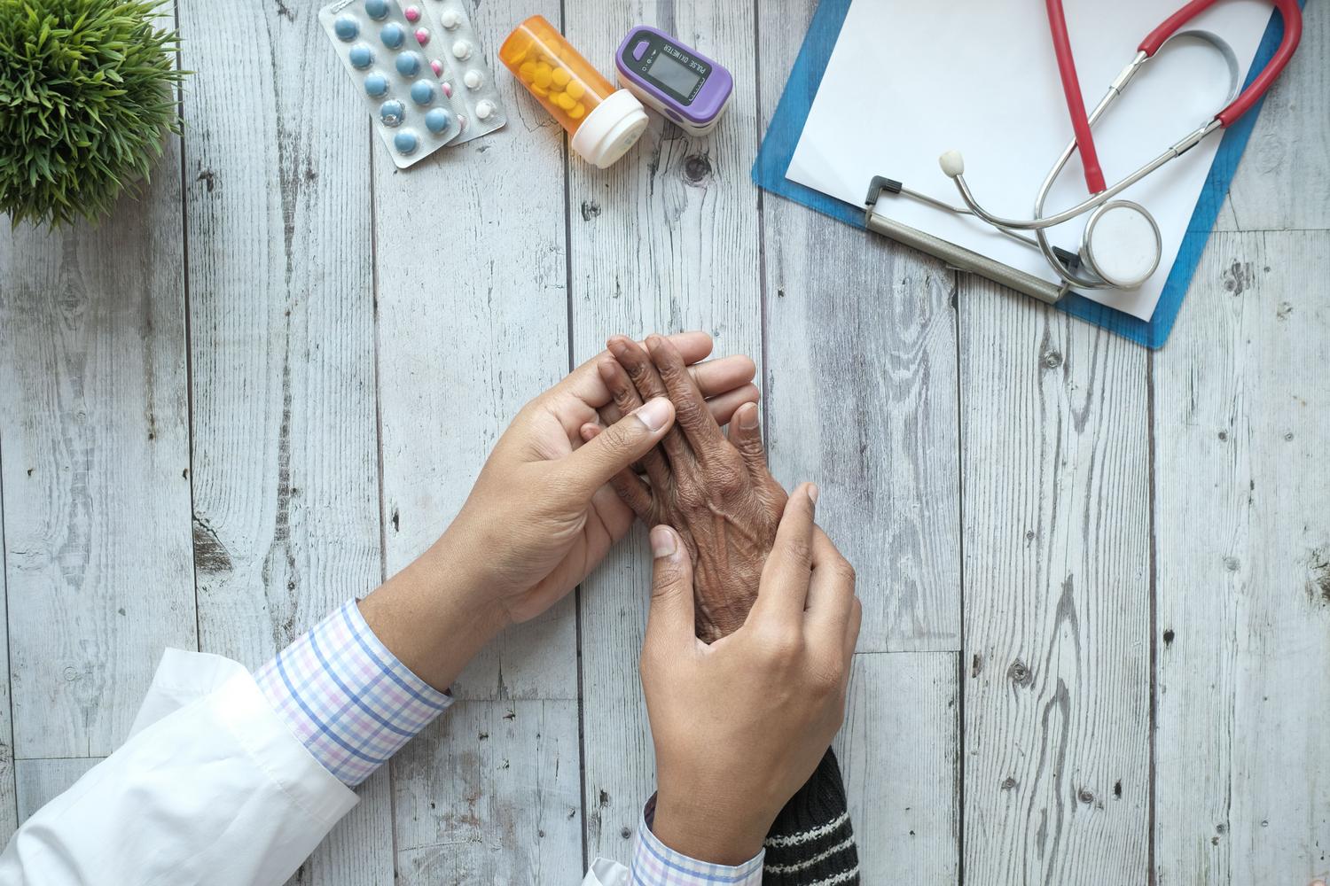 Médico sosteniendo las manos de un paciente anciano, representando el cuidado y la vulnerabilidad en el diagnóstico de la artritis reumatoide